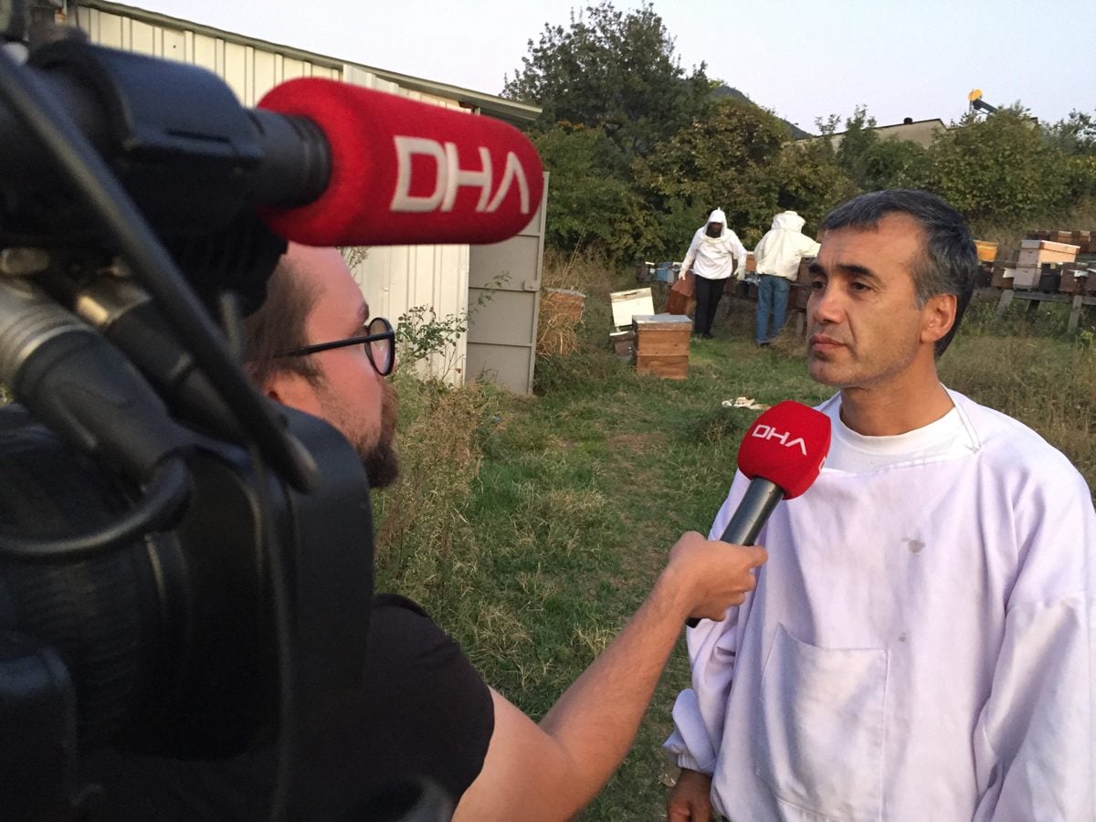Kovanların yanında arı kıyafetli bir arıcı ve bir haber ekibinin mikrofonu